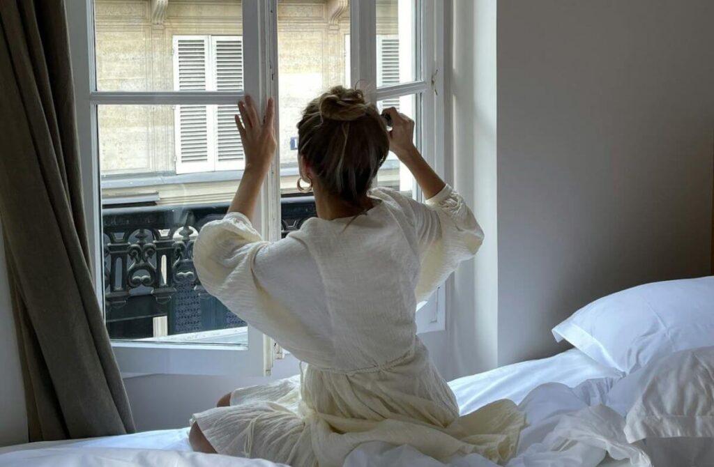 Expressions de Fréquence : Choisissez la Bonne Expression pour Chaque Contexte Femme en peignoir blanc assise sur son lit face à une fenêtre à Paris
