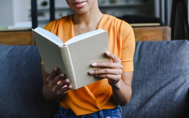Femme noire assise sur un canapé qui lit un livre