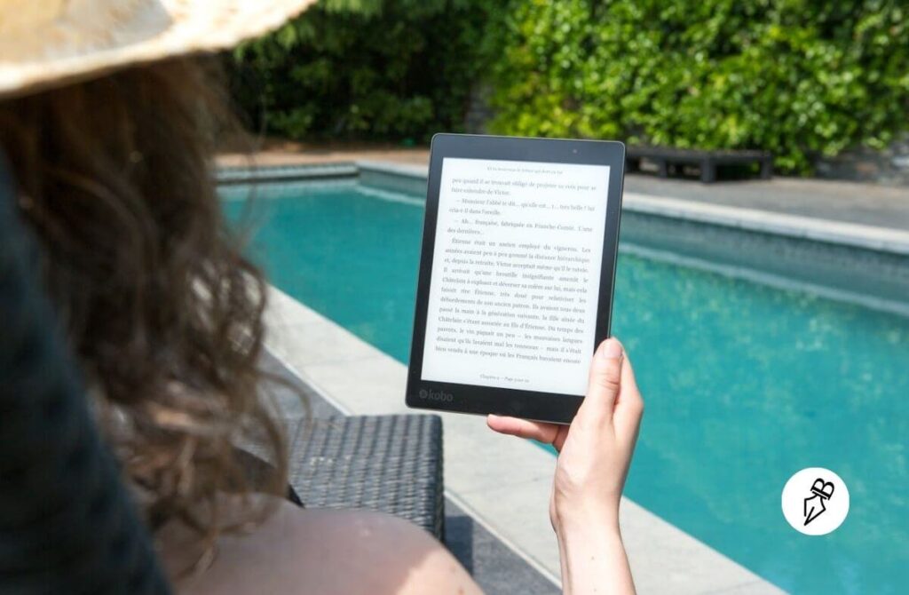 Liseuse en Voyage : 7 Raisons Convaincantes d’emporter votre e-reader plutôt que des livres papier Femme Assise à Côté De La Piscine Tenant Une Liseuse