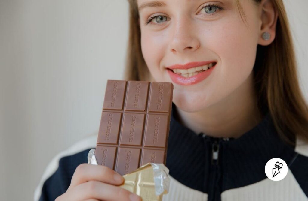 Jeune femme aux yeux bleus avec le sourire qui tient une plaque de chocolat dans sa main.